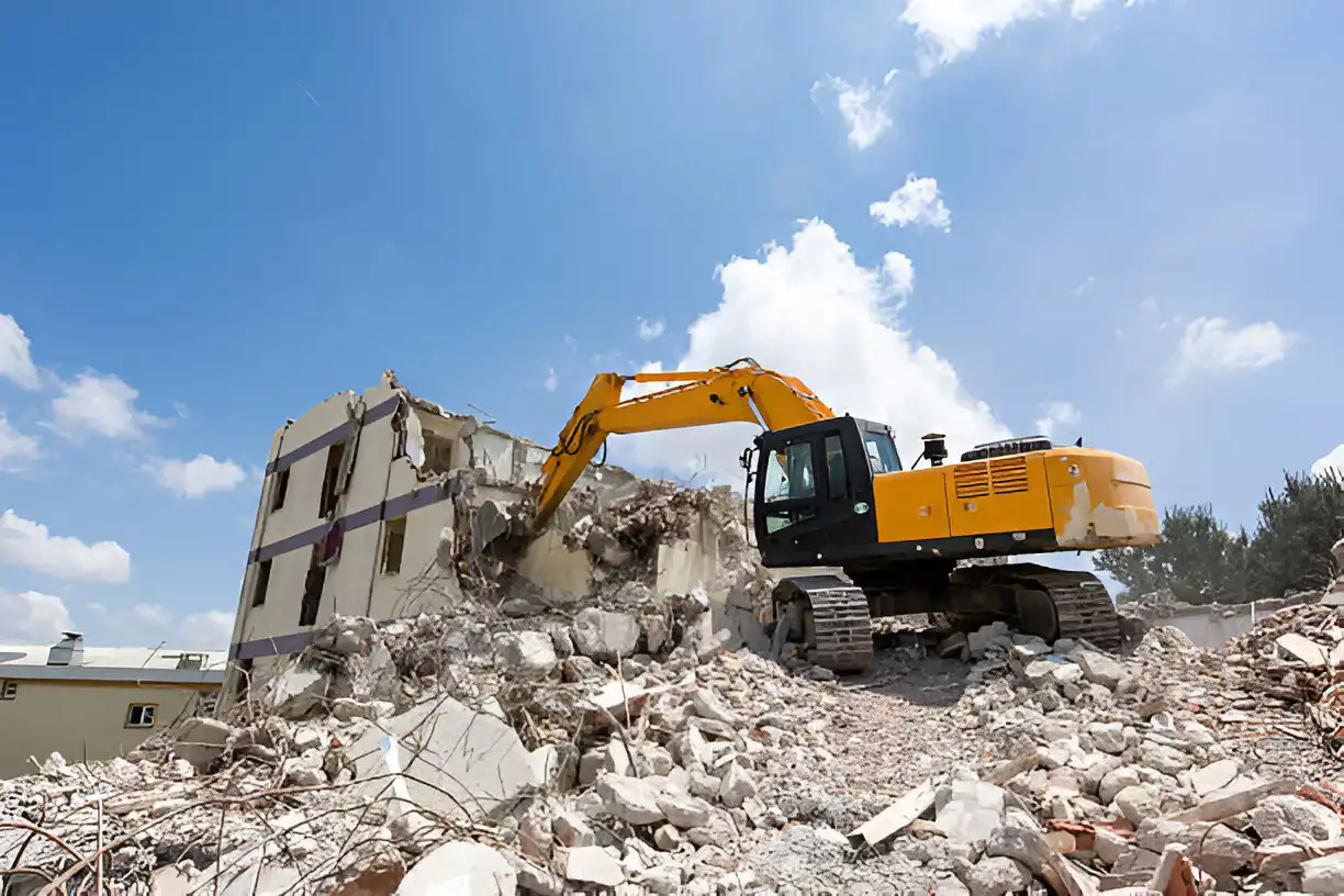 Yellow excavator tearing down a multi-story building amidst rubble under a clear blue sky, showcasing professional demolition and removal services.