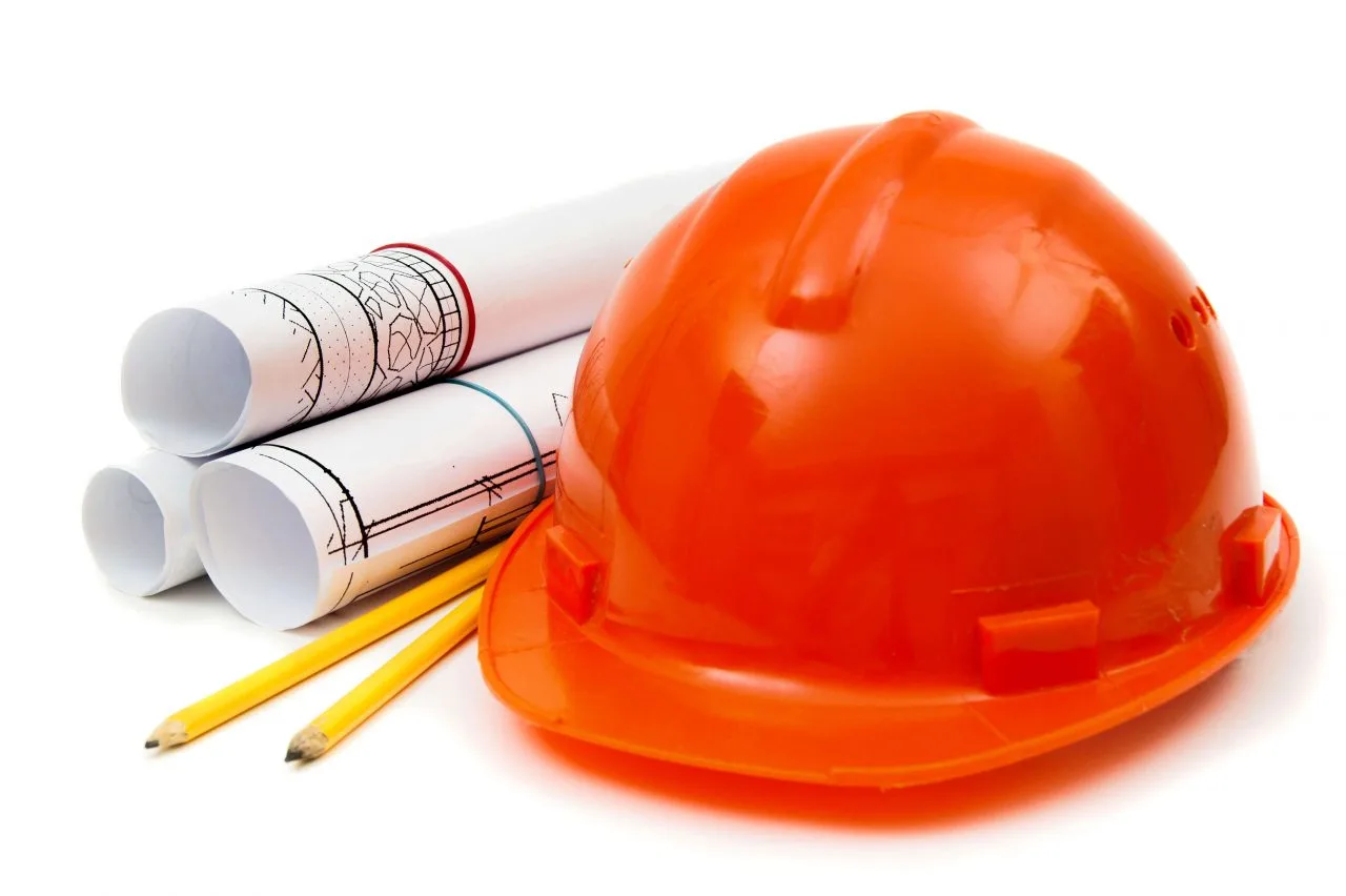 An orange safety helmet alongside rolled architectural blueprints and pencils, symbolizing construction planning and safety measures in demolition and removal projects.