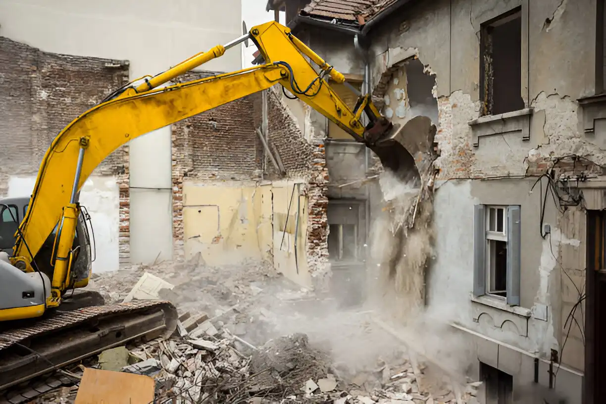 A yellow excavator demolishing an old brick and plaster building, with debris and dust in the foreground, showcasing demolition and removal services.