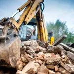 Yellow excavator bucket crushing concrete rubble at demolition site
