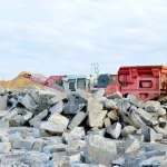 Pile of concrete rubble with a red rock crusher at a demolition site.