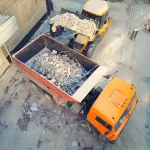 Overhead shot of construction waste being loaded into dumpster by heavy equipment at work site