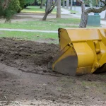 Yellow wheel loader clearing dirt in landscaped urban construction site