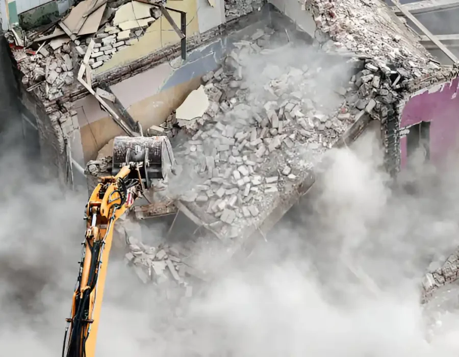 Bird's eye view of yellow excavator arm demolishing building interior amid thick gray dust clouds