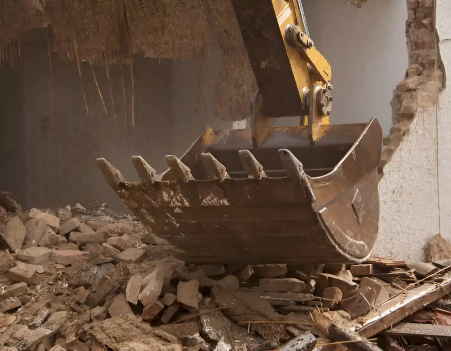 Heavy-duty excavator bucket with teeth positioned over brick and concrete debris during interior demolition work