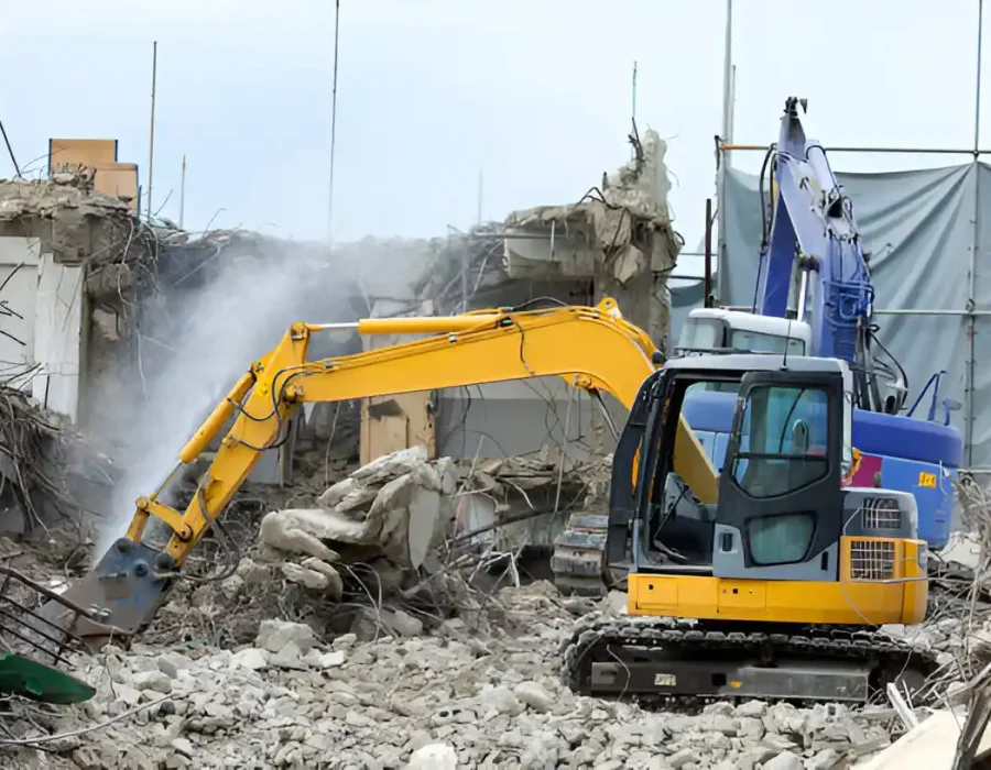 Yellow excavator performing building demolition with debris removal and concrete crushing at construction site