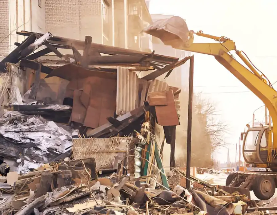Yellow excavator dismantling wooden debris, industrial demolition site, scattered wreckage