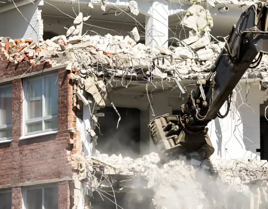 Hydraulic excavator breaking down brick and concrete building with dust clouds