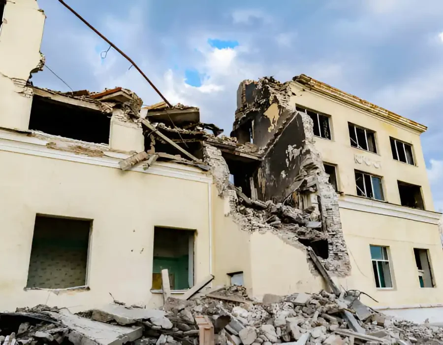 Damaged yellow building with partial collapse, debris scattered, blue sky background
