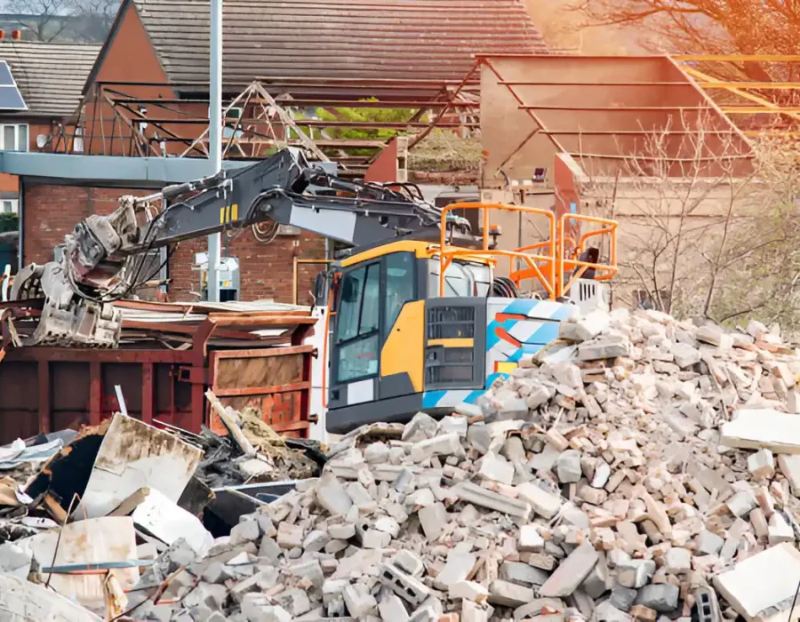 Excavator clearing construction site with large pile of concrete rubble and debris