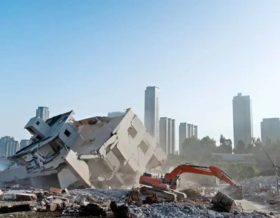 Large excavator demolishing multi-story building with city skyline in background