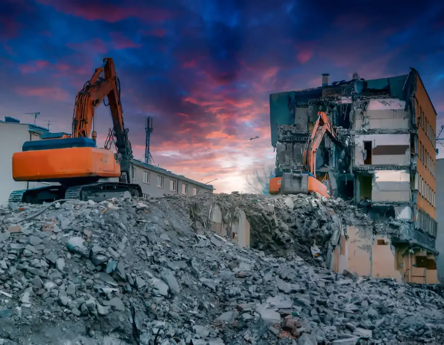 Two excavators demolishing multi-story building with dramatic sunset sky backdrop