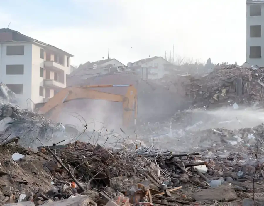 Excavator demolishing multi-story buildings with dust control spray in action