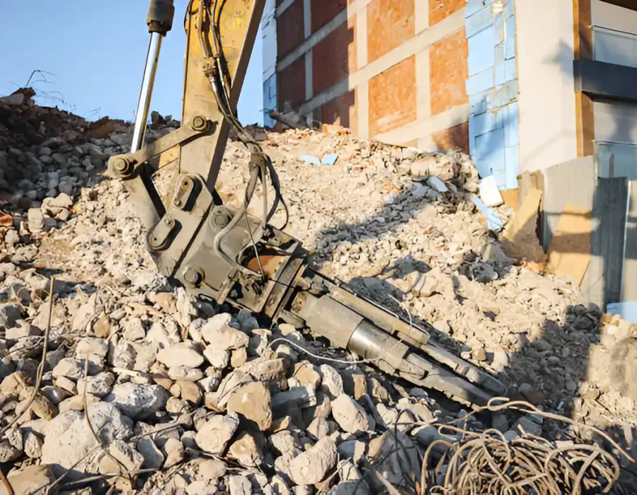 Excavator hydraulic attachment breaking concrete debris near building wall
