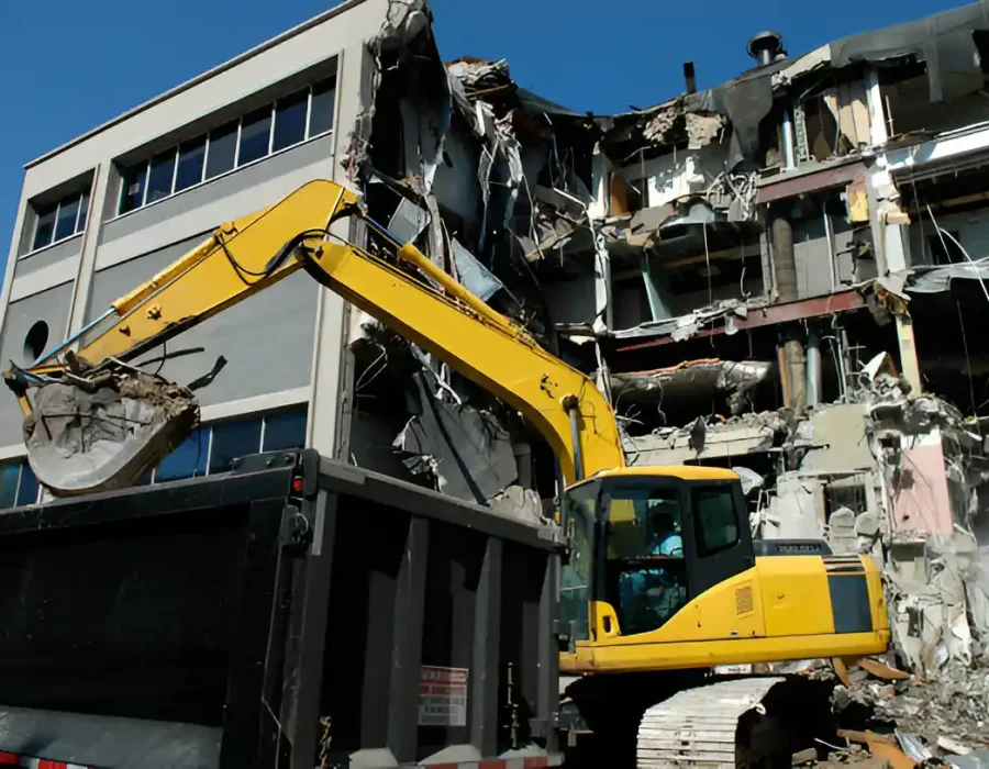 Yellow excavator dismantling concrete office building with structural damage