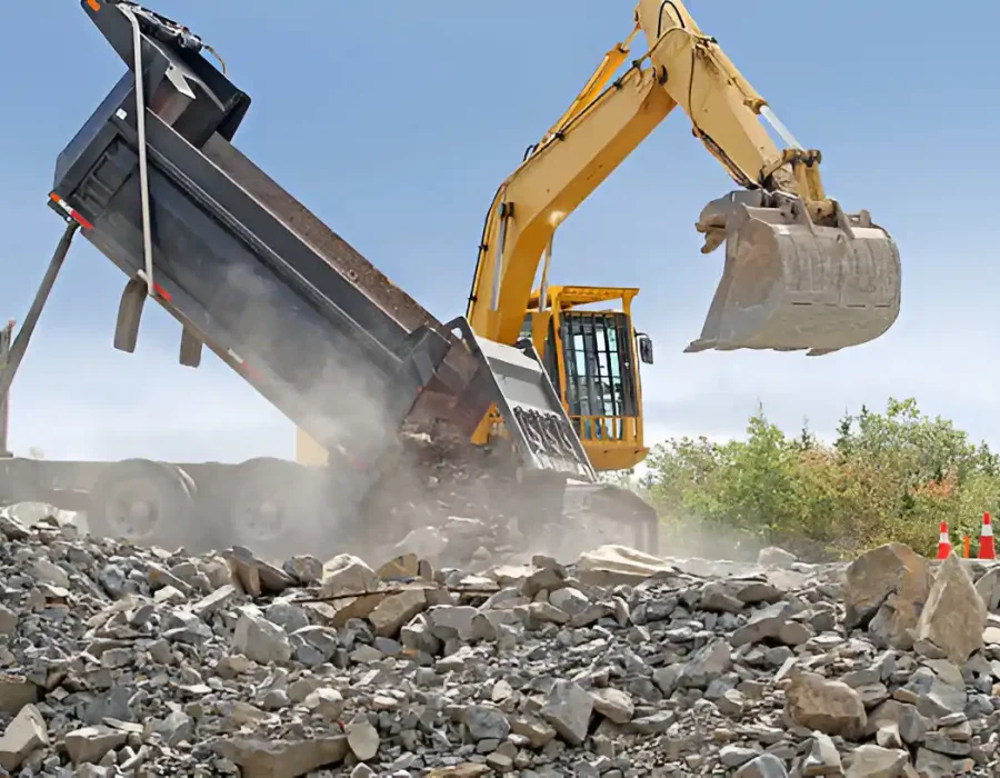 Excavator transferring rubble into a dump truck at a demolition site for debris removal and cleanup.