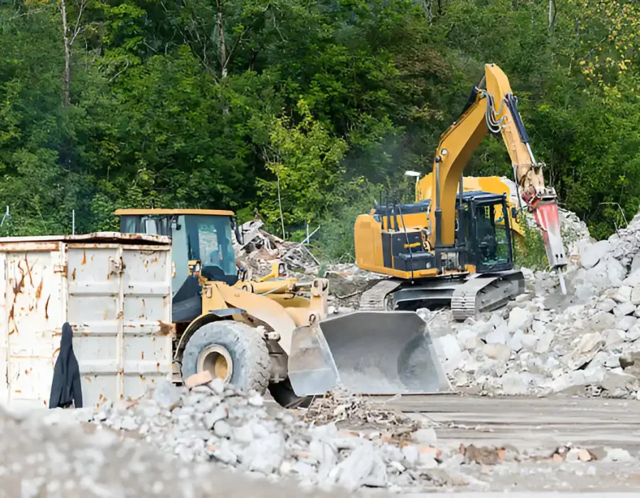 Excavators and loader removing rubble at a demolition site with trees in the background.