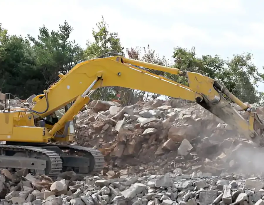 Yellow excavator breaking rocks during demolition work at a construction site.