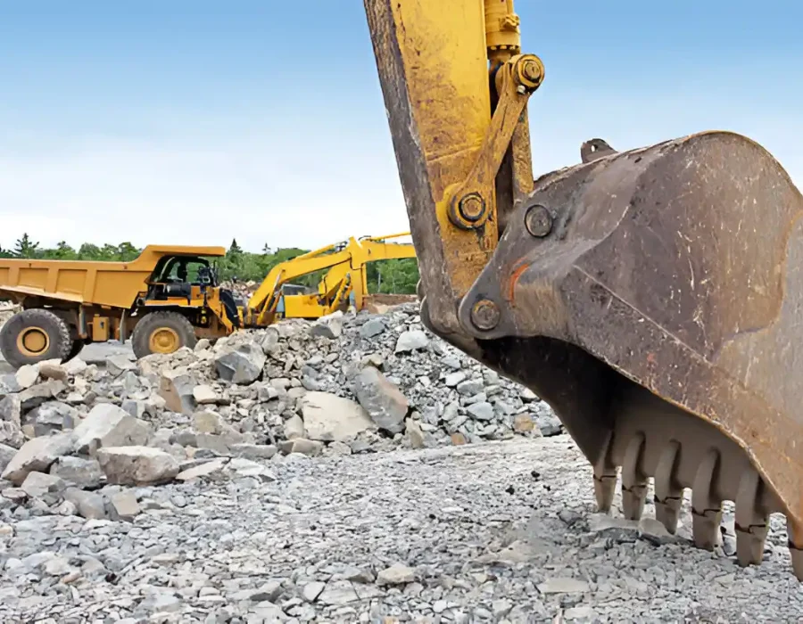 Excavator bucket and dump truck at a rocky demolition site.