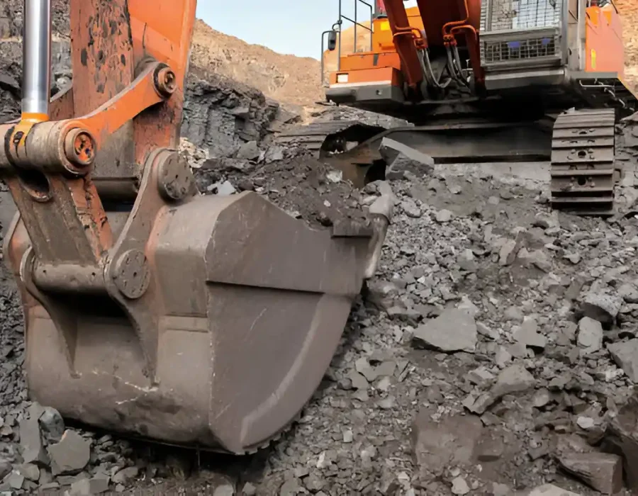 Orange excavator bucket processing rocky rubble at industrial demolition site
