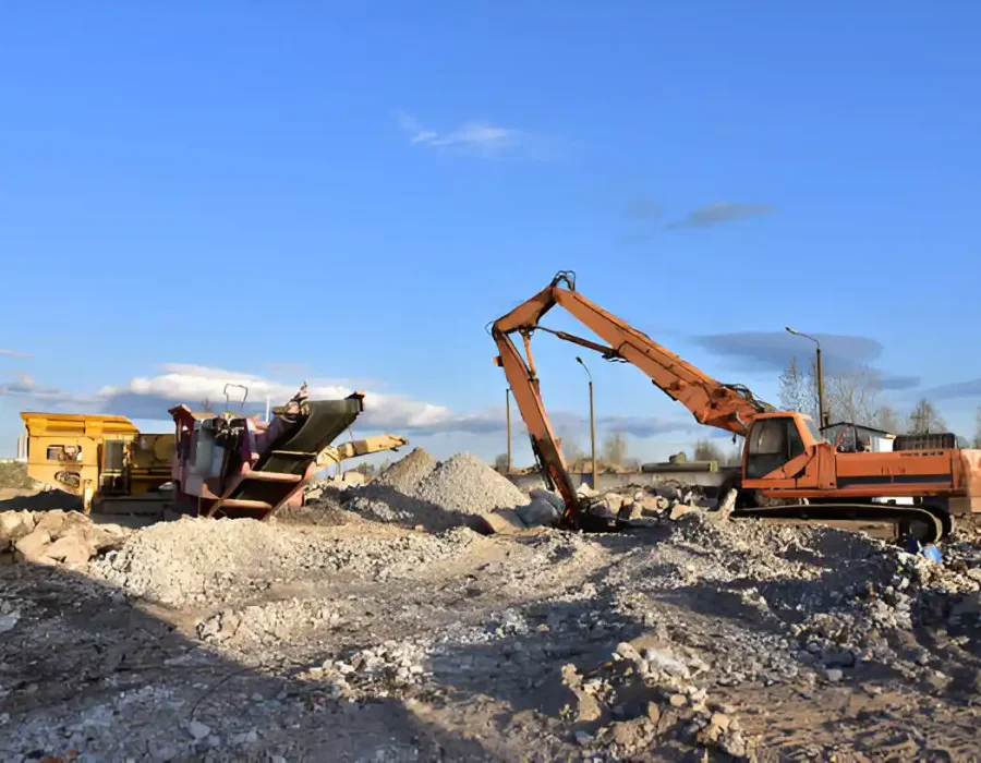 Excavators and crusher processing debris at a demolition site under a clear blue sky.