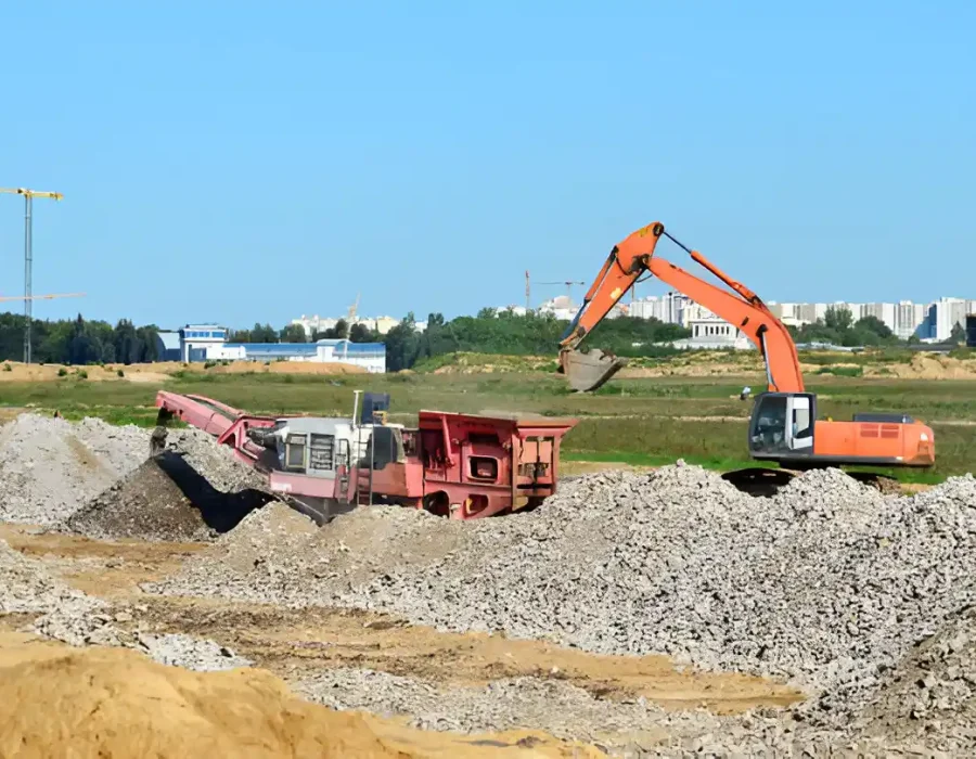 Excavator and debris crusher processing rubble on a construction site under a clear blue sky.
