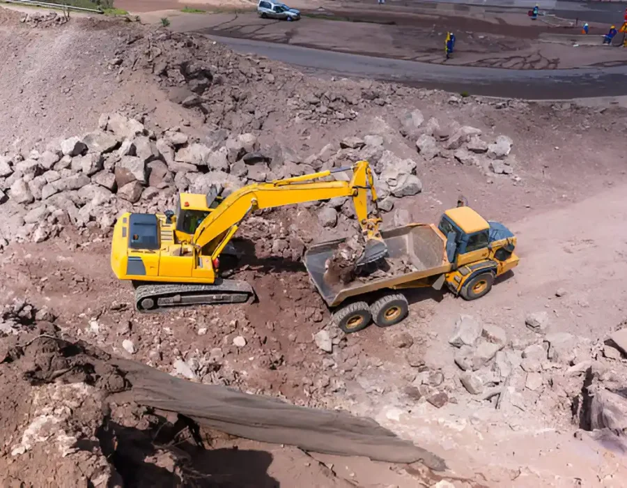Excavator loading construction debris into a dump truck at a demolition site.