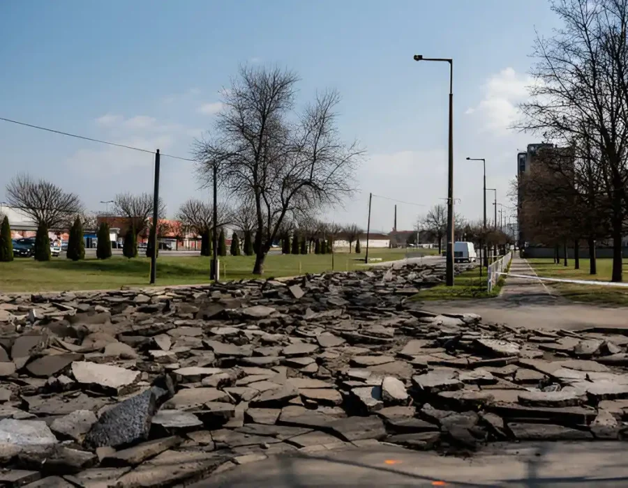 Broken concrete rubble in urban parking area with trees and streetlights