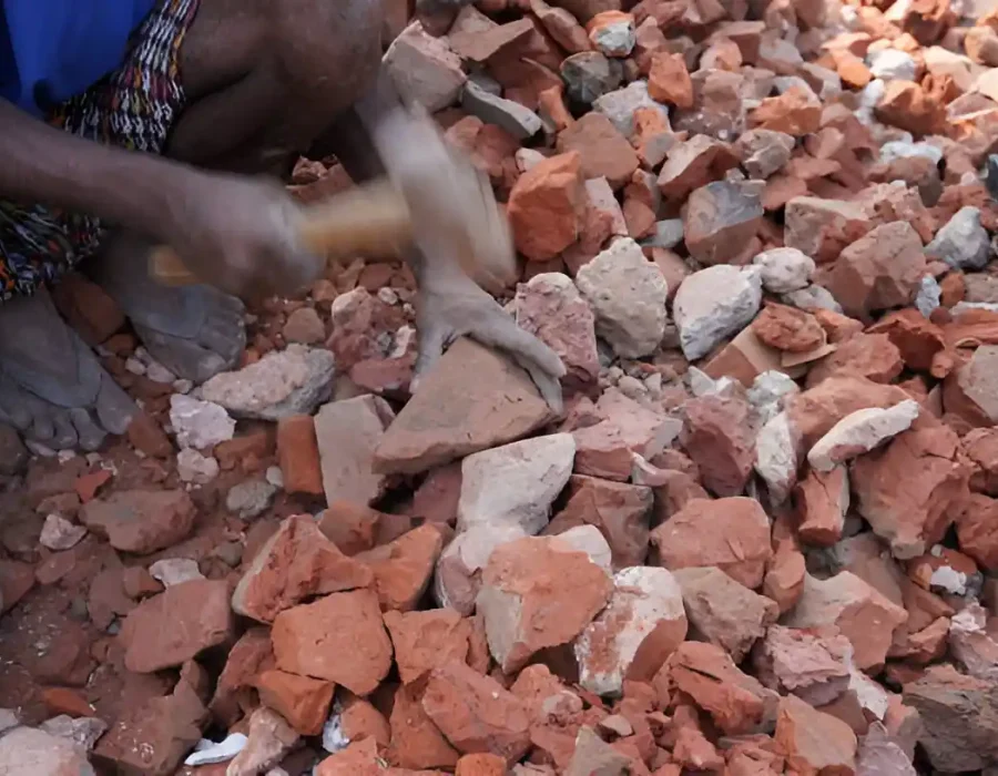 Worker breaking bricks with a hammer for debris removal and site cleanup.