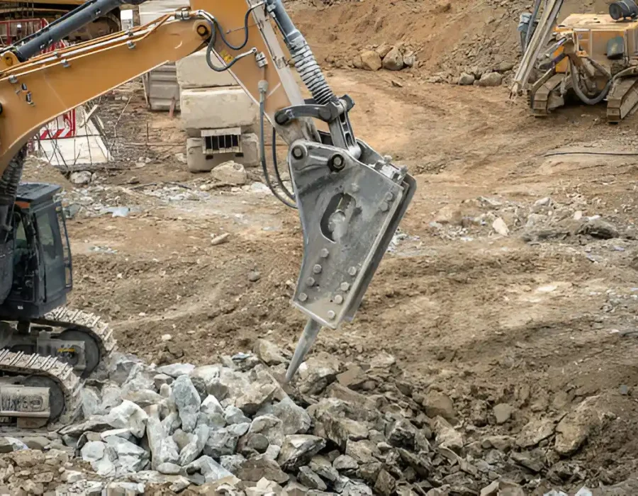 Excavator with hydraulic breaker crushing rocks at a construction site for debris removal.