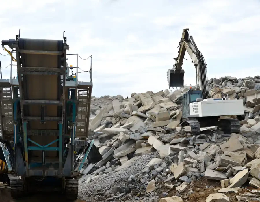 Excavator loading concrete rubble into a crusher machine at a demolition and debris removal site.
