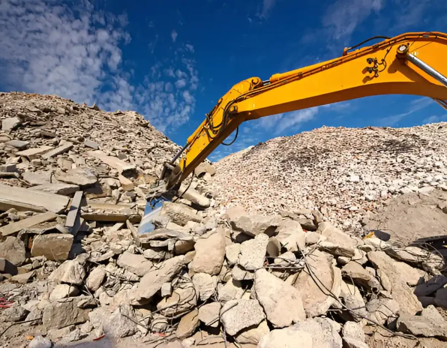 Excavator arm working on a large pile of rubble at a demolition site under a clear blue sky.