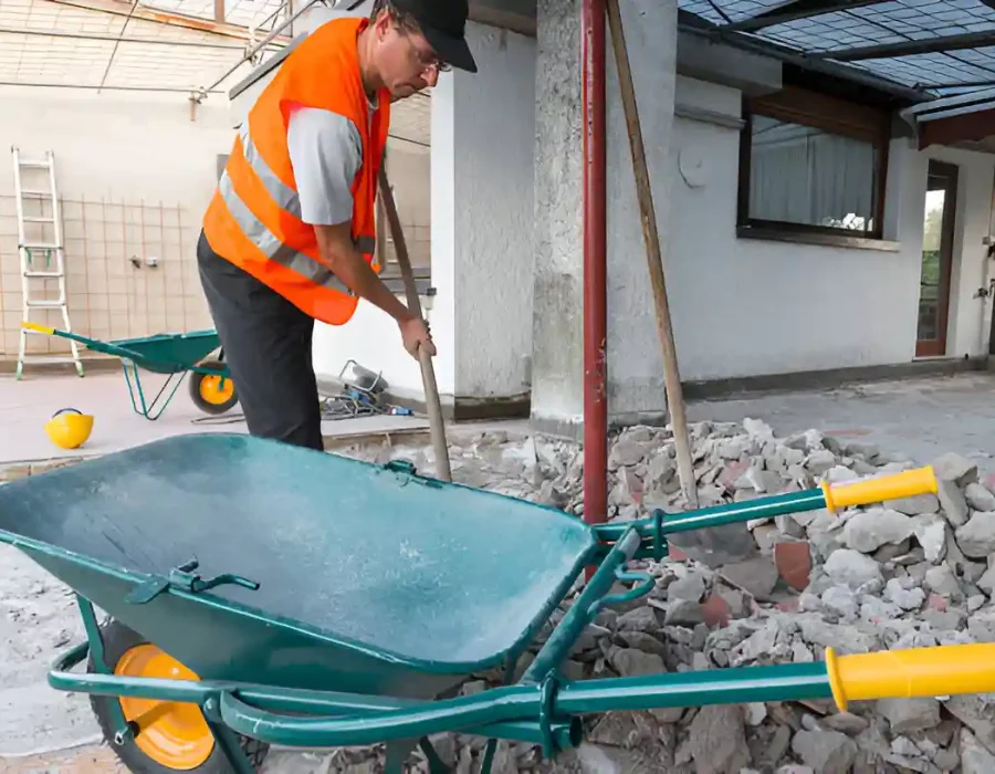 Worker in safety vest clearing construction debris with wheelbarrow during interior demolition project cleanup