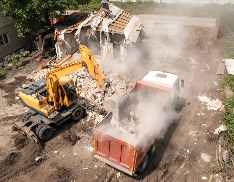 Aerial view of excavator loading demolition waste into red container during house teardown
