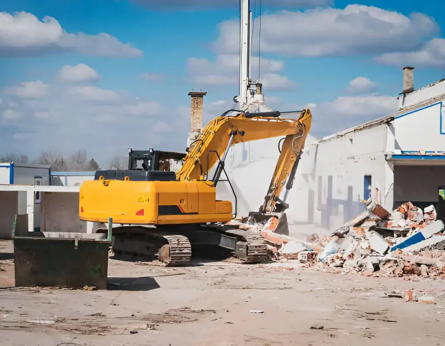 Yellow tracked excavator at commercial demolition site with sorted construction debris