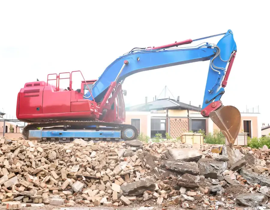 Red and blue excavator working on large pile of sorted demolition rubble at construction site