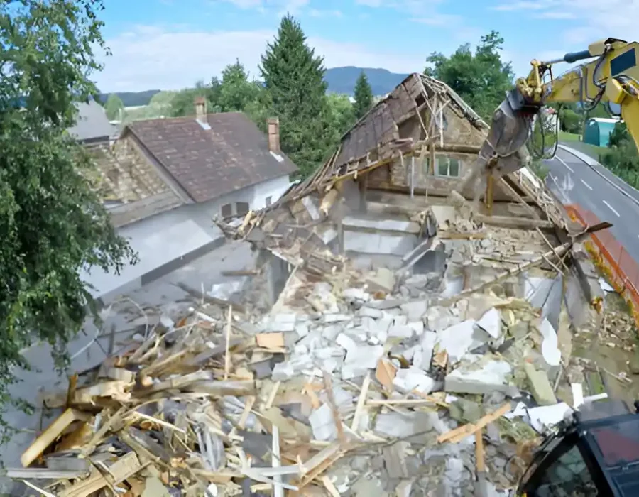 Excavator demolishing house roof with mixed construction debris in suburban neighborhood