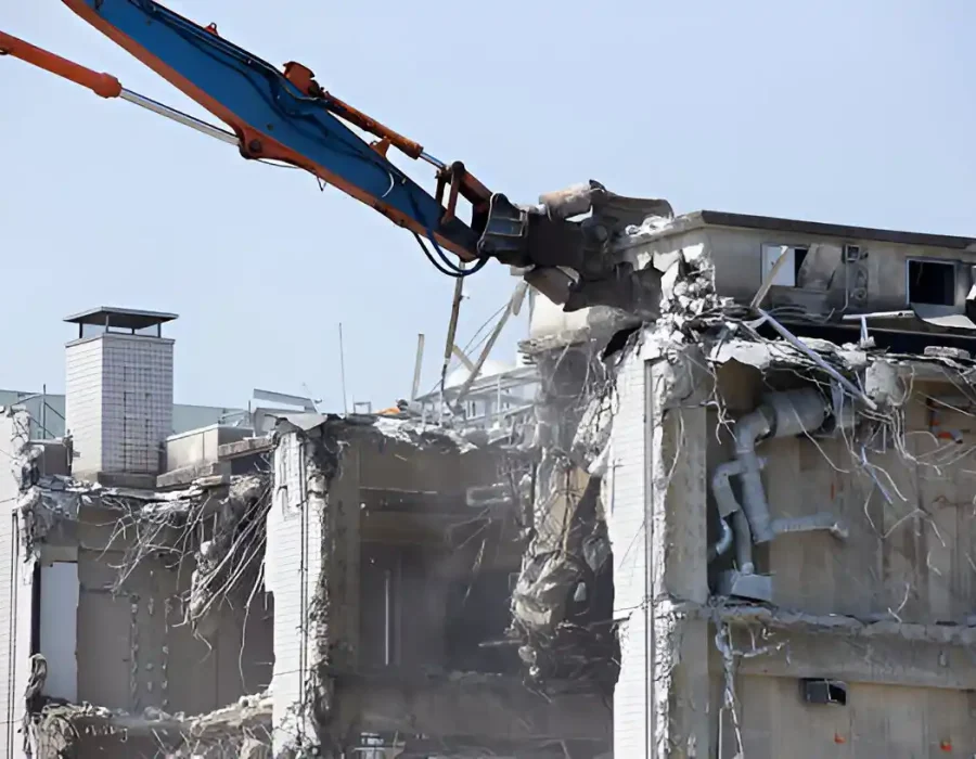 High-reach demolition equipment breaking concrete walls with exposed rebar and interior structure