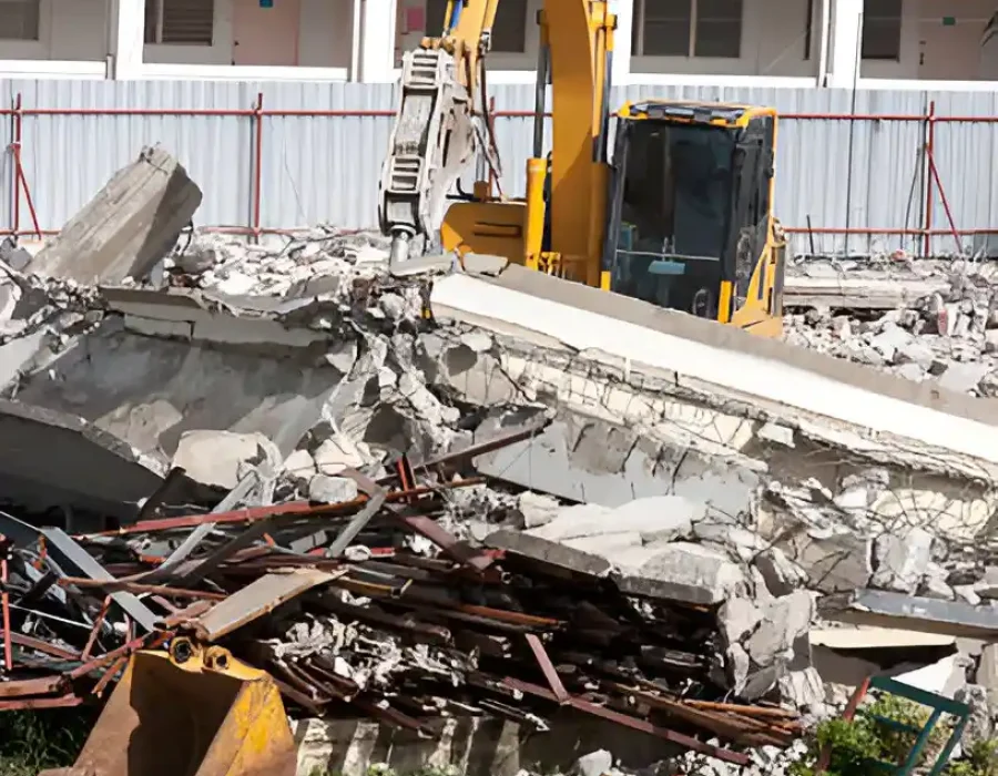 Yellow excavator separating concrete and metal debris during multi-story building demolition