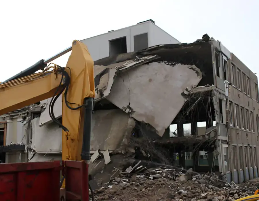 Excavator demolishing multi-story commercial building with debris collection container