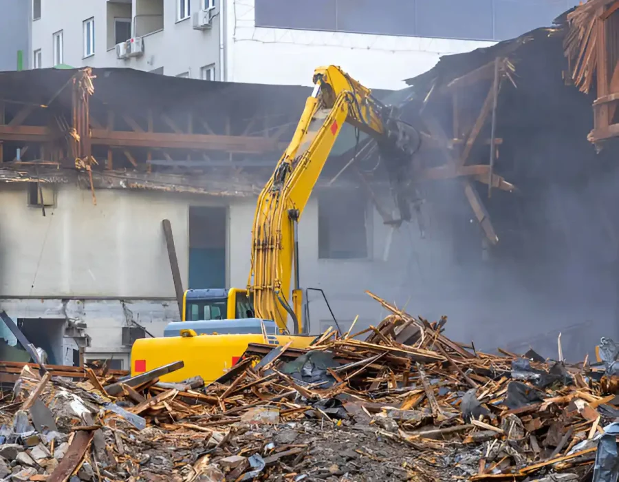 Yellow excavator managing large pile of mixed wood and building debris during demolition