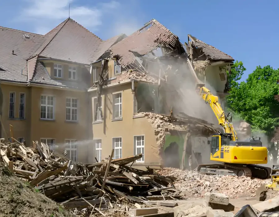 Excavator demolishing large heritage building with sorted debris piles and dust suppression