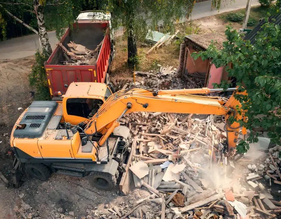 Orange excavator loading mixed demolition debris into red dumpster truck for disposal
