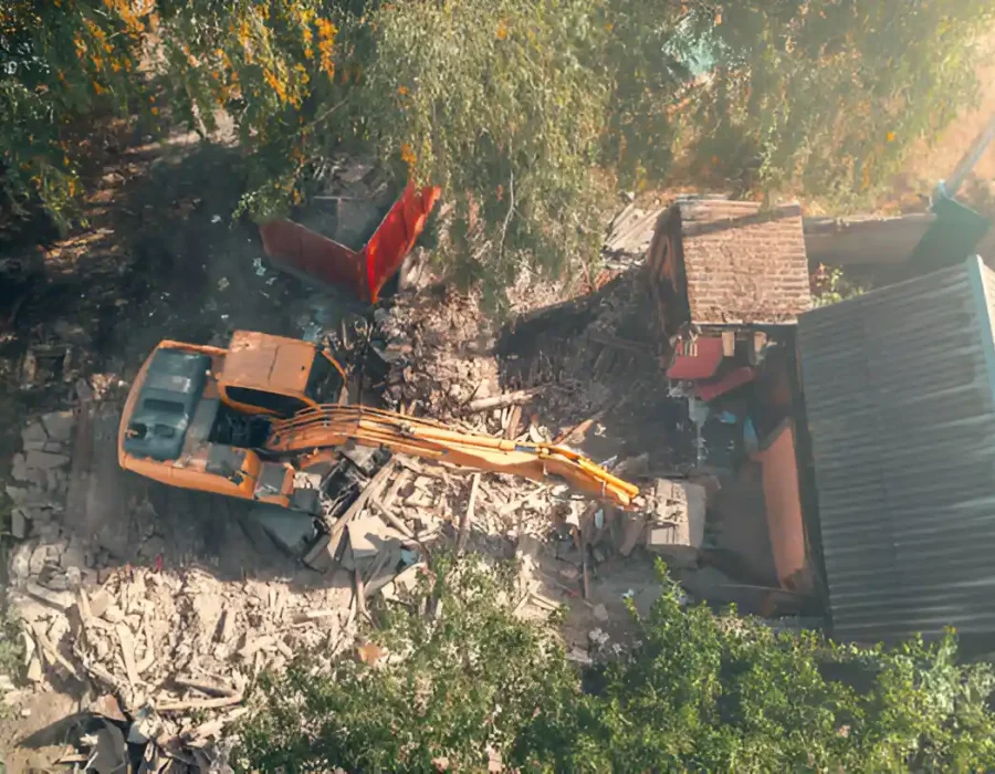 Bird's eye view of excavator clearing demolition debris among trees at residential site