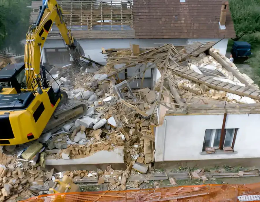 Aerial view of yellow excavator demolishing single-story house with mixed construction debris