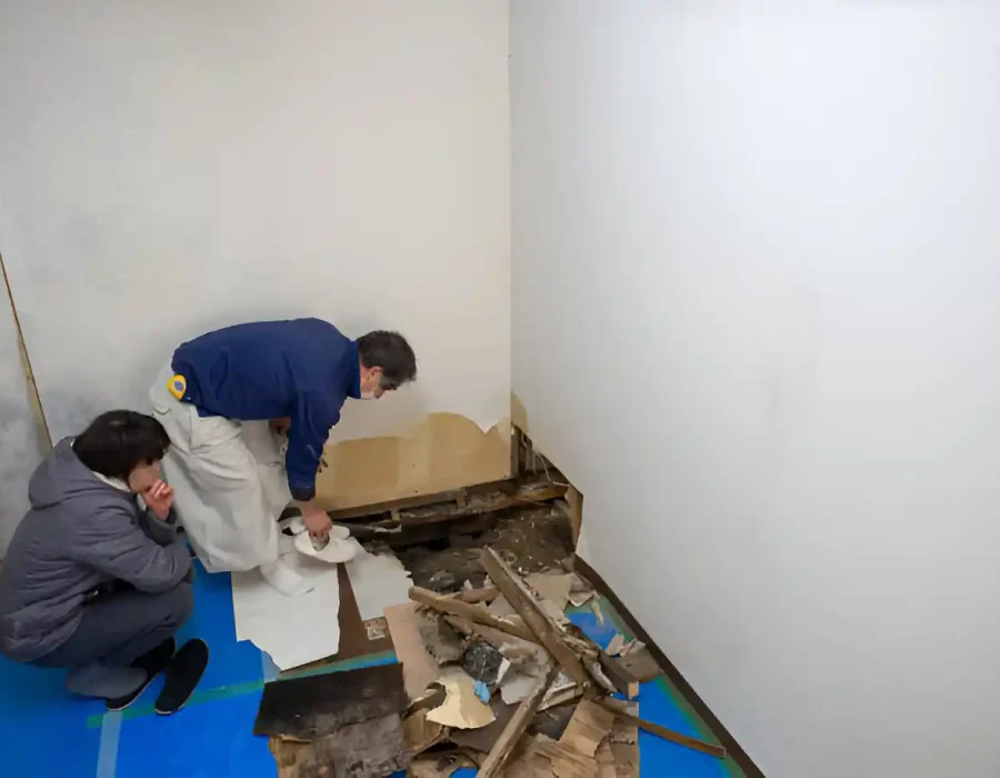 Two people examine wall damage with debris on the floor before demolition work begins.