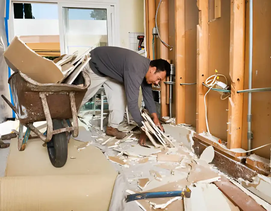 Demolition contractor removing drywall debris with wheelbarrow during bathroom renovation project