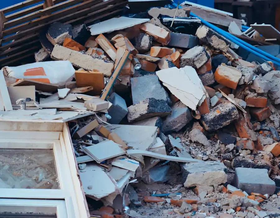 Demolition debris pile including broken window frames, bricks, and construction materials in dumpster