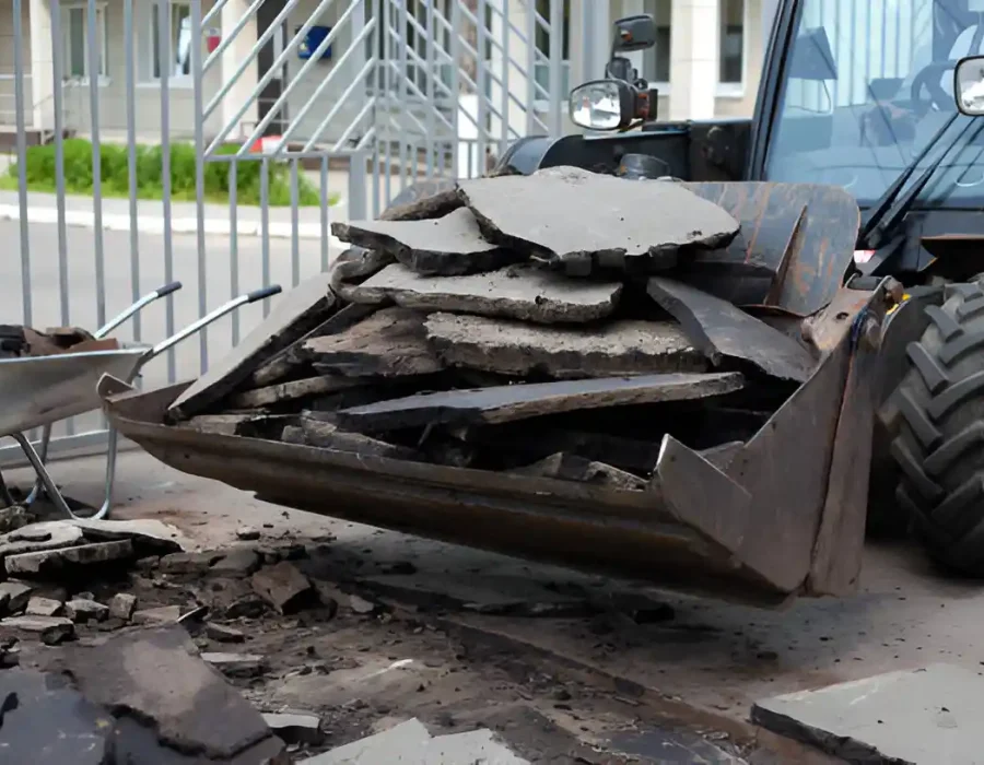 Heavy equipment bucket filled with broken concrete slabs and wheelbarrow at demolition site