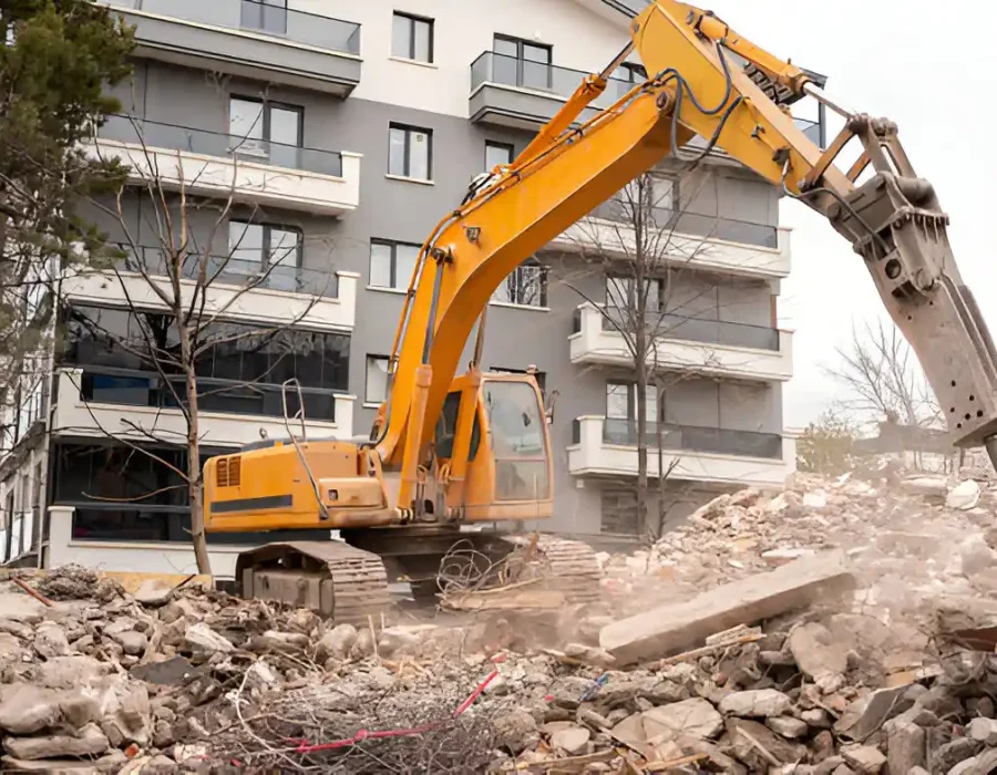 Yellow excavator with hydraulic breaker attachment demolishing concrete at urban construction site